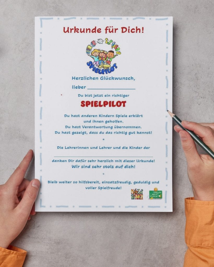 Auf der Urkunde steht „Urkunde für Dich!“ und „Spielpilot“ in kräftiger roter Schrift, eingerahmt von blau-weißen Elementen und Spielillustrationen.